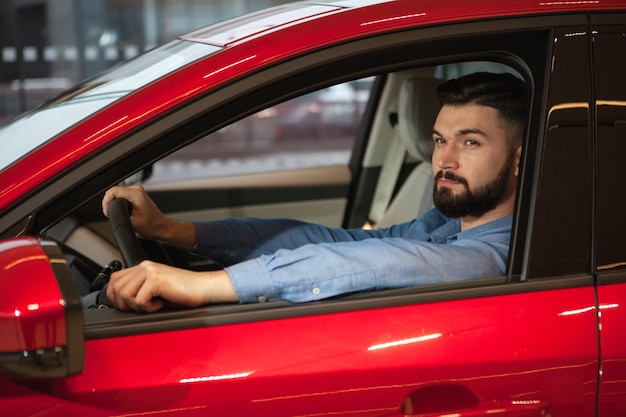 ディーラーで新しい自動車に座っている魅力的なひげを生やした男