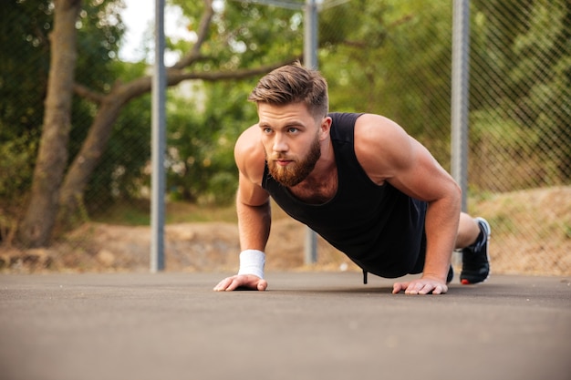 Attractive bearded young sportsman doing push-ups outdoors