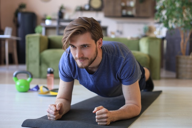 Attractive beared man doing plank exercise at home during quarantine. Fitness is the key to health.