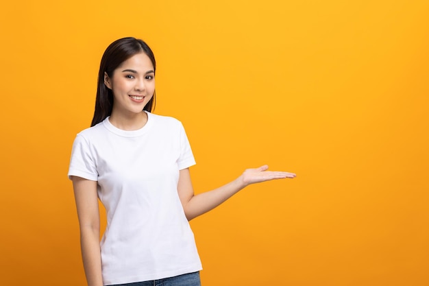 Attractive Beautiful asian woman open hands palm up holding something. Surprised happy female on isolated yellow background.