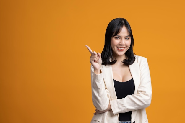 Attractive Beautiful asian woman pointing finger into blank space. Smiling female on isolated yellow background.