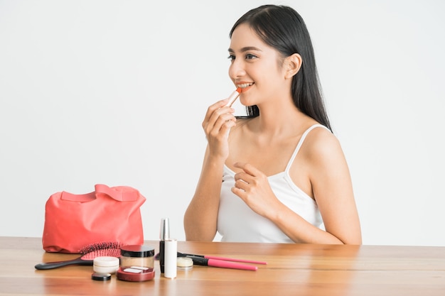 Attractive beautiful mixed race asian woman applying lipstick on her lips over white wall