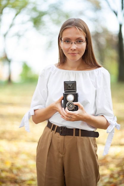 写真 秋の公園でレトロなビンテージ二眼レフ反射カメラを保持している魅力的な美しい少女