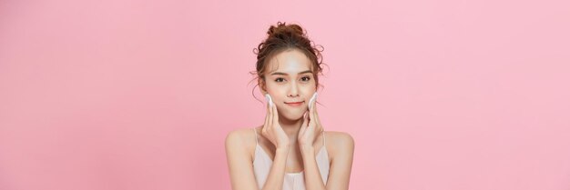 写真 ピンクの背景にメイクを落とす綿パッドで魅力的な美しい若いアジア人女性のきれいな肌