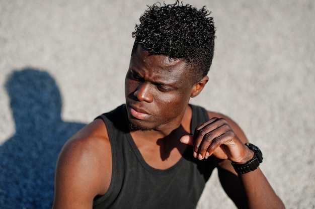 Attractive black african american guy in black muscle shirt posing on the pile of gravel in industrial zone.