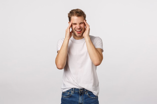 頭痛に苦しんでいる白いtシャツで魅力的な金髪のひげを生やした男