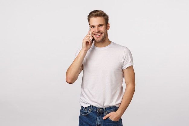 Attractive blond bearded man in white T-shirt talking to the phone