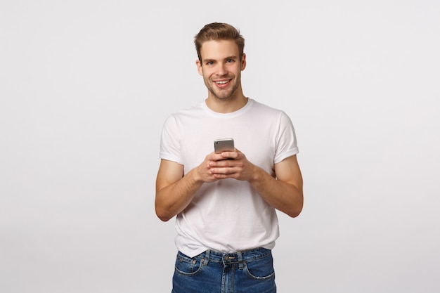 Привлекательный белокурый бородатый мужчина в белой футболке с помощью смартфона