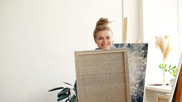 Attractive blonde artist happy with her work, the artist holds her painting in her hands