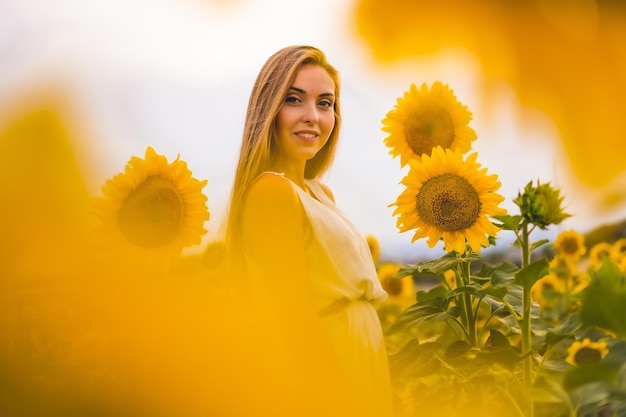 Attractive blonde female in a white dress posing in a sunflower field