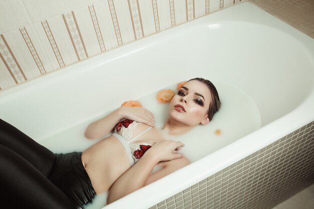 Attractive blonde model with bright makeup takes a bath with milk and roses