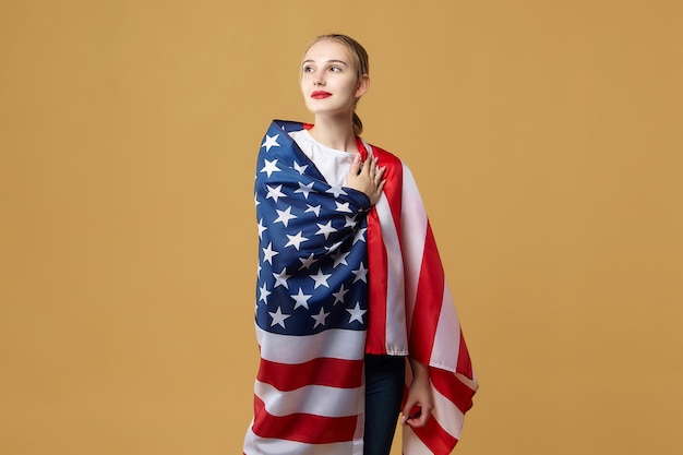 Photo attractive blonde proudly poses with an american flag. photo shoot in the studio on a yellow background.