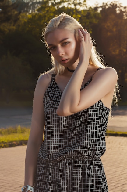 Attractive blonde woman in black romper posing at the city in rays of sun