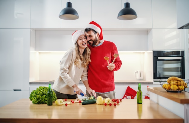 Attractive blonde woman cutting cucumber while her boyfriend is hugging her