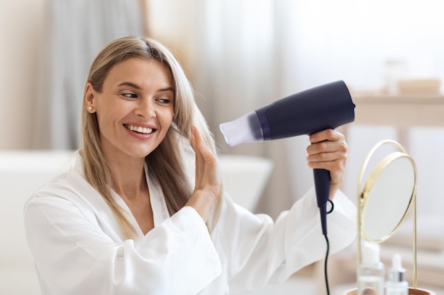 Attractive blonde woman using hair dryer at home