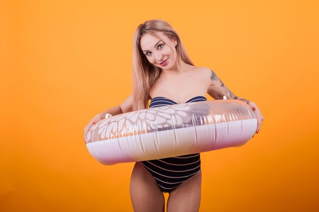 Attractive blonde woman wearing swimming suit ready for the beach over yellow background. Holding inflatable swim ring.