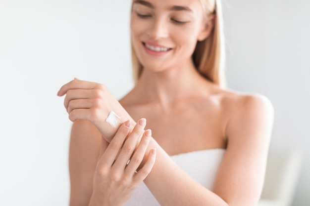 Photo attractive blonde young lady applying lotion to arms in bathroom