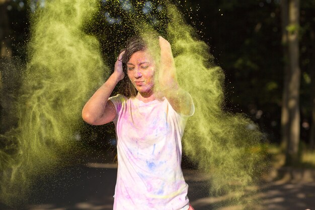 Foto attraente donna asiatica bruna che si diverte con la vernice holi che esplode intorno a lei