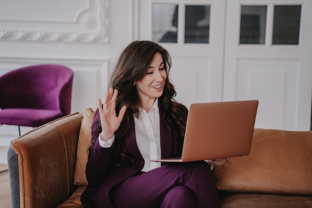 Attractive brunette businesswoman in violet suit and white shirt makes video call using laptop