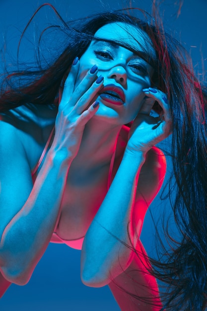 Attraente modella bruna su sfondo blu studio in luce al neon