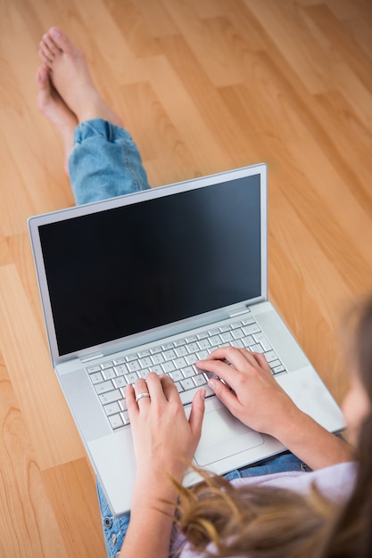 Attraente bruna seduta sul pavimento usando il suo computer portatile