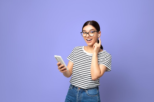 Attractive brunette in striped tshirt using small white wireless headphones against color background