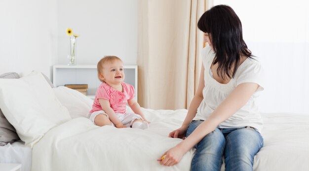 Attraente donna bruna godendo un momento con il suo bambino mentre era seduto su un letto