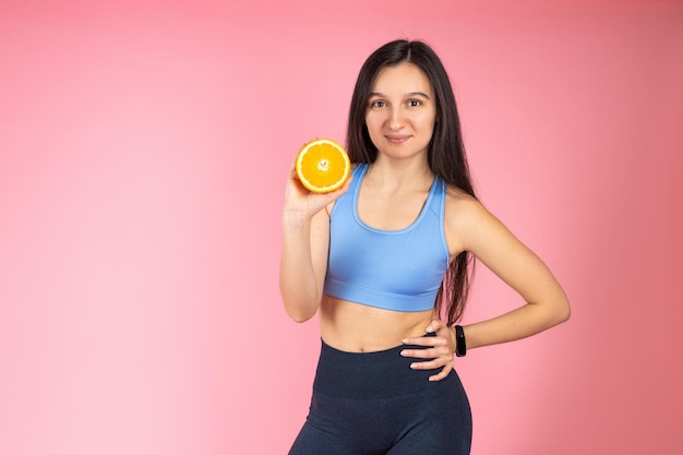 Foto attraente donna bruna in abbigliamento sportivo alla moda con frutta arancione su sfondo rosa concetto di stile di vita sano indoor studio shot dieta agrumata