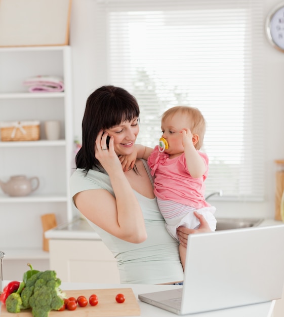 Attractive brunette woman on the phone while holding her baby in her arms