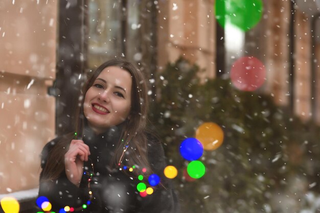 Attractive brunette woman walking at the street near the colorful garlands with snowflakes. Space for text