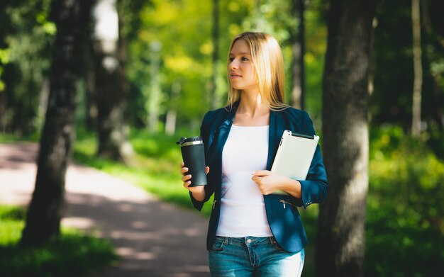 Attractive business girl using her tablet, drinking coffee in the park