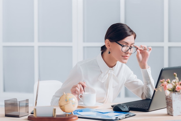 Attraente donna d'affari in bicchieri che lavorano alla scrivania in ufficio