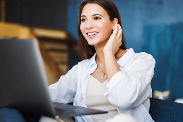 Attractive business woman sits at table in laptop, smartphone lies on table, makes notes with pencil in notebook.