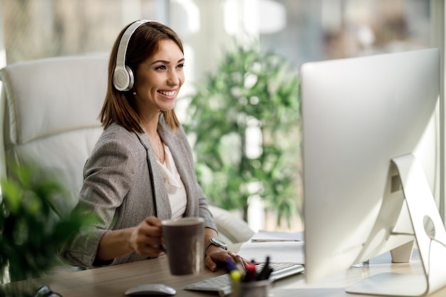 An attractive business woman sitting alone in her home office with headphones and working on computer.