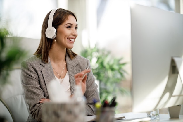 An attractive business woman sitting alone in her home office with headphones and working online at computer.