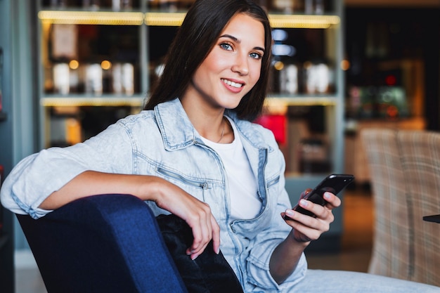 Attractive business woman sitting on armchair in cafe, home office. Close-up portrait. Beautiful brunette girl smiling