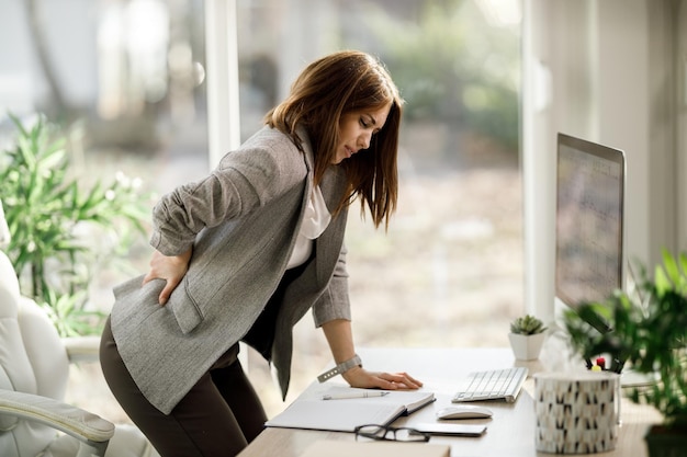Foto una donna d'affari attraente che soffre di mal di schiena mentre lavora al computer in un ufficio moderno.