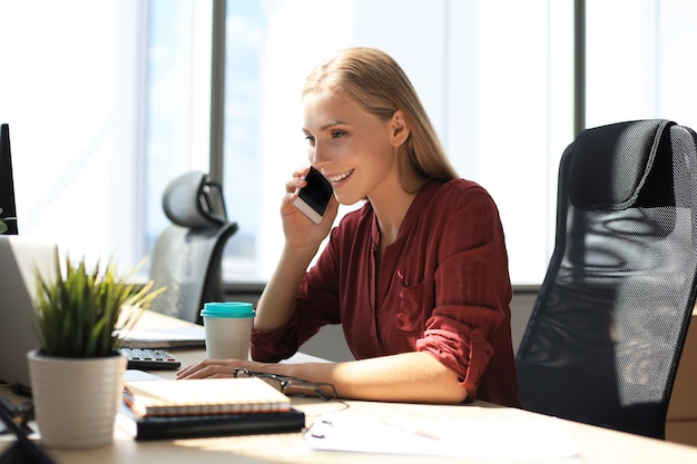 Attractive business woman talking with collegues on the mobile phone while sitting in the office desk.