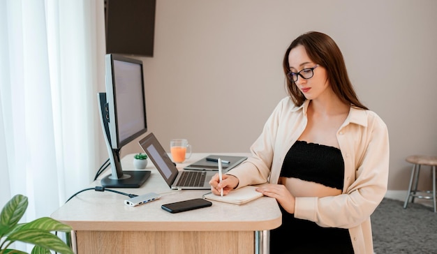 Attractive business woman wearing casual clothes working at home office on laptop and making notes Young happy female student studying in online university