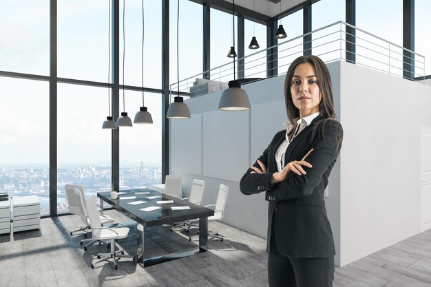 現代的なオフィスのインテリアに立っている腕を折った魅力的なビジネス女性