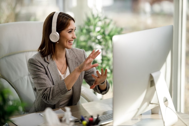 An attractive business woman with headphones and using a computer to have a web conference at home office.