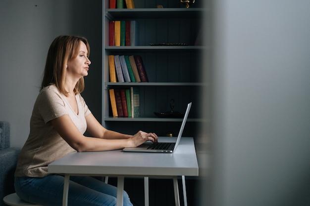 Attractive business woman working on laptop computer from home office sitting at desk in living room looking on screen