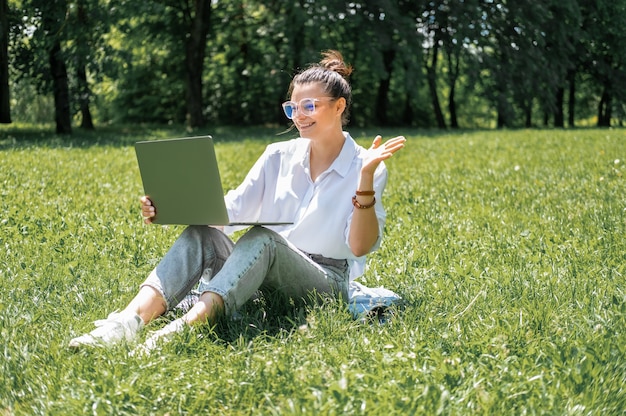 Attractive business women in glasses and white blouse using laptop sitting on grass on break.