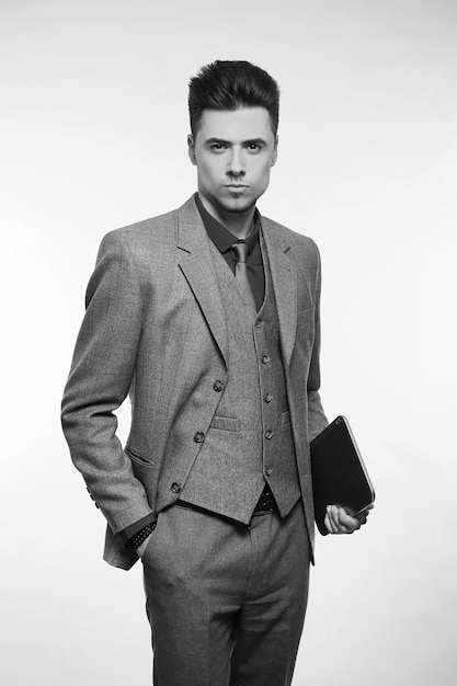 Attractive businessman smiling and holding his tablet while wearing a red tie and blue suit standing on white studio background