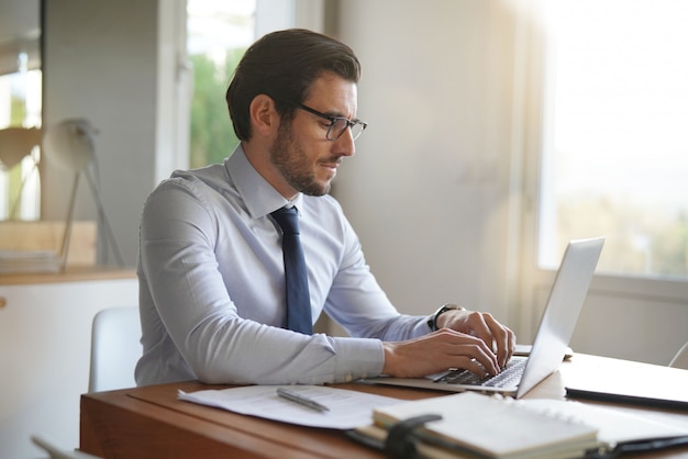 Attractive businessman typing on laptop in modern office