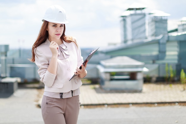 Attractive businesswoman in beige suit stand on the roof and hold tablet