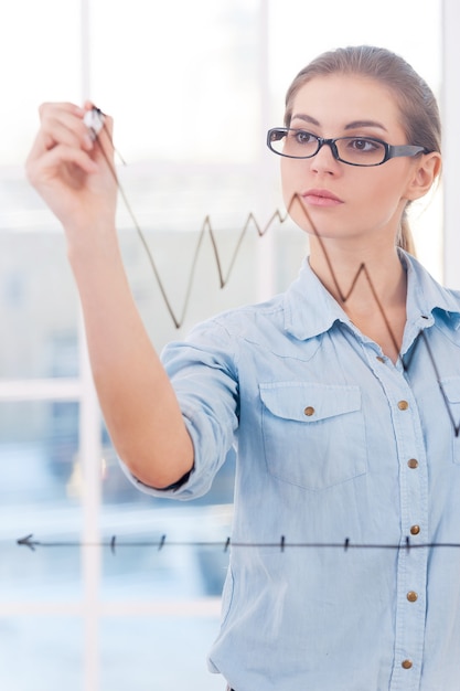 Attractive businesswoman drawing a graph. An attractive businesswoman analyst drawing a graph on a clear class wall