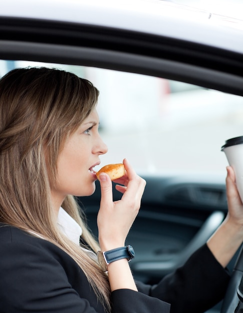 Attractive businesswoman eating and holding a drinking cup while driving