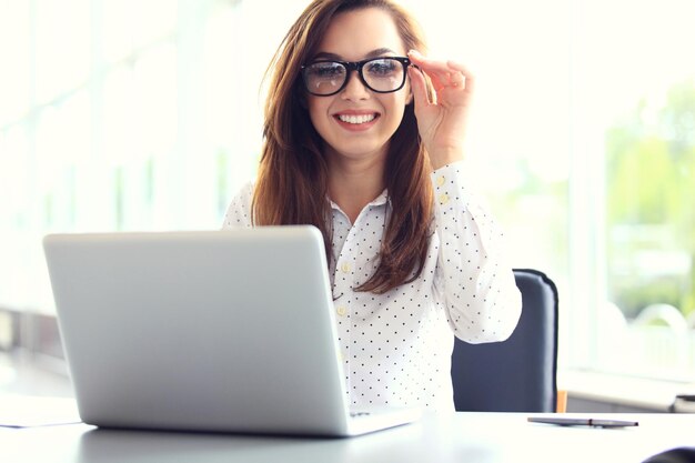 Attractive businesswoman sitting on a desk with laptop in the office