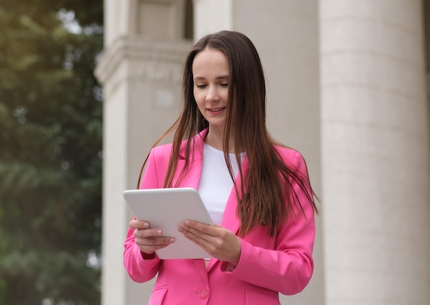 Attractive businesswoman using a digital tablet while sitting in front of business building